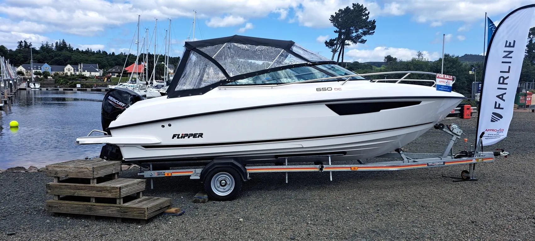 A white Flipper 650 DC boat on a trailer at a marina, with a "For Sale" sign and a blue sky with clouds in the background.